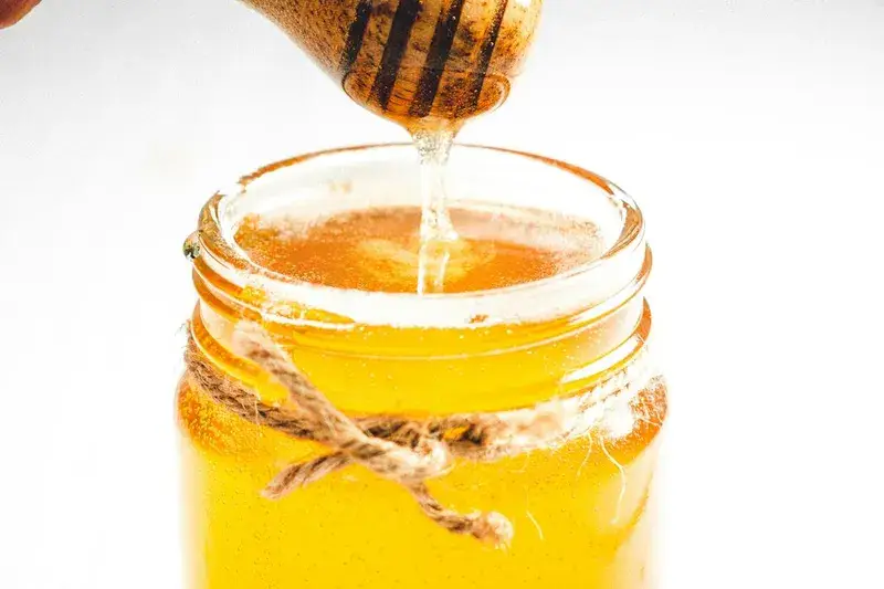 Goldener Honig tropft von einem Löffel in ein Glas