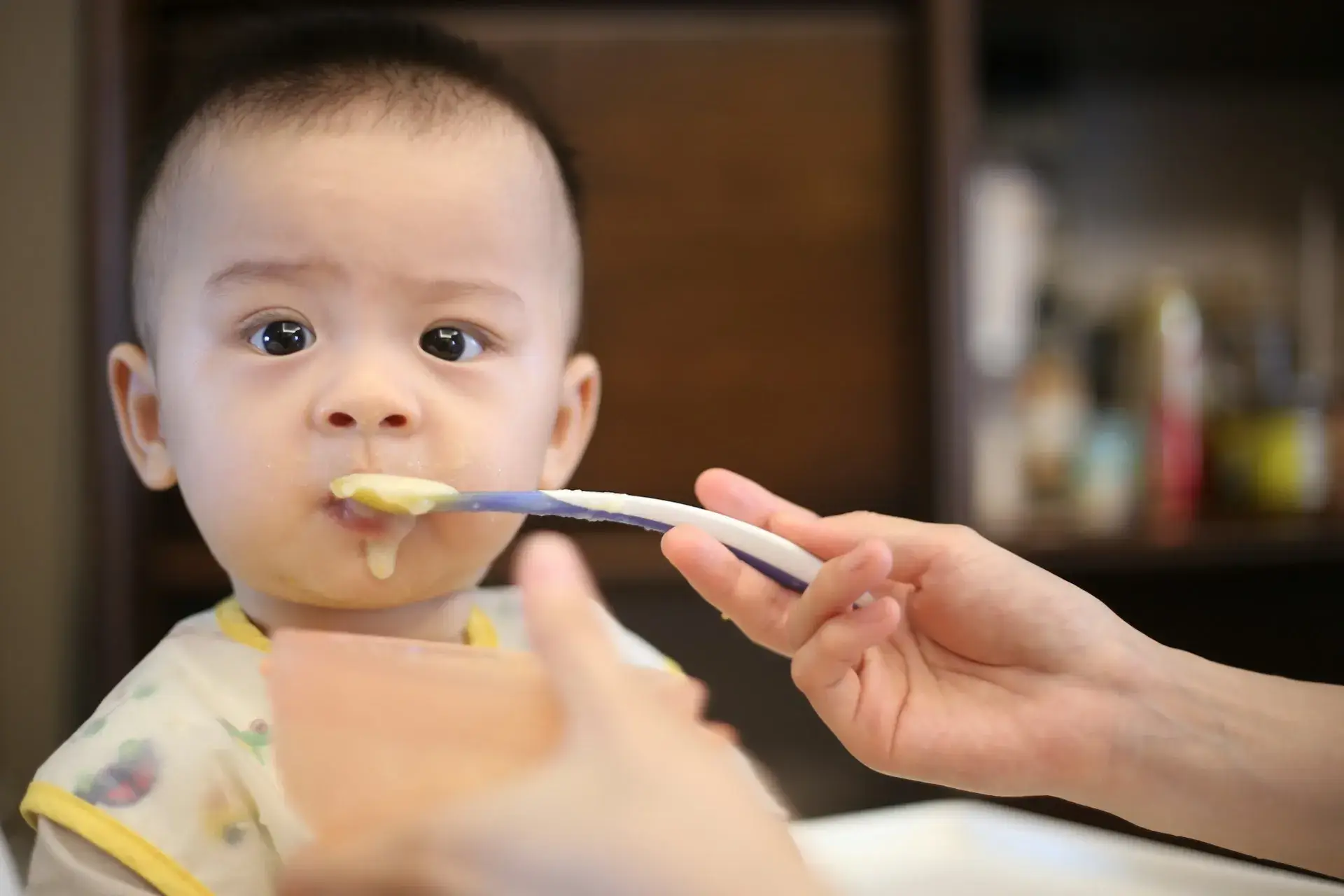 Baby im Hochstuhl wird mit dem Löffel gefüttert